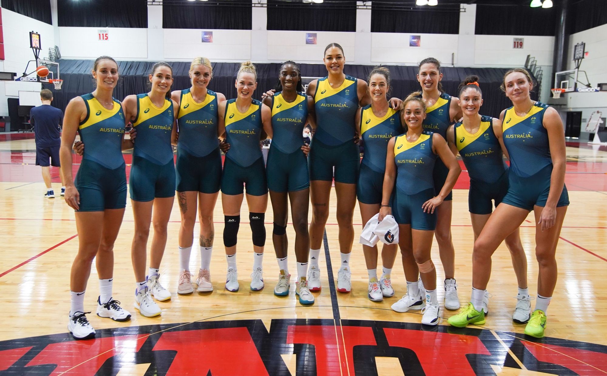 A photo of the members of the Australian Opals basketball team lined up on a court, wearing their green and yellow bodysuits.